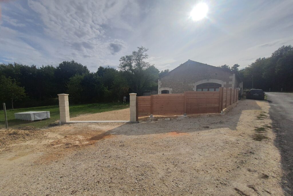 Nouveaux piliers de portail en pierre et clôture bois sur chemin de gravier devant une maison rurale en pierre. Matériaux de construction.