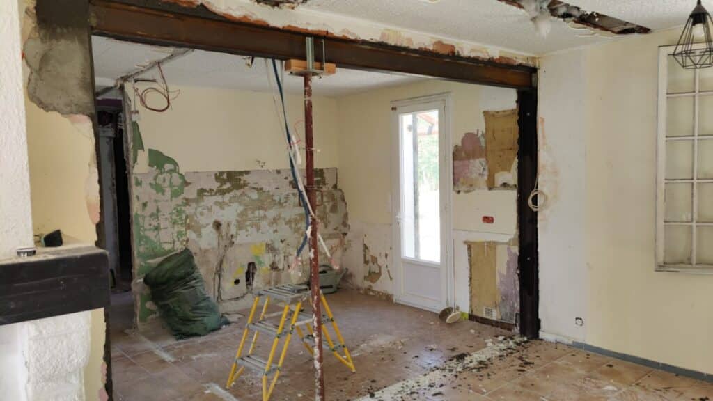 Chantier de rénovation avec pose de poutre IPN, étai de soutien et murs décapés dans une maison.