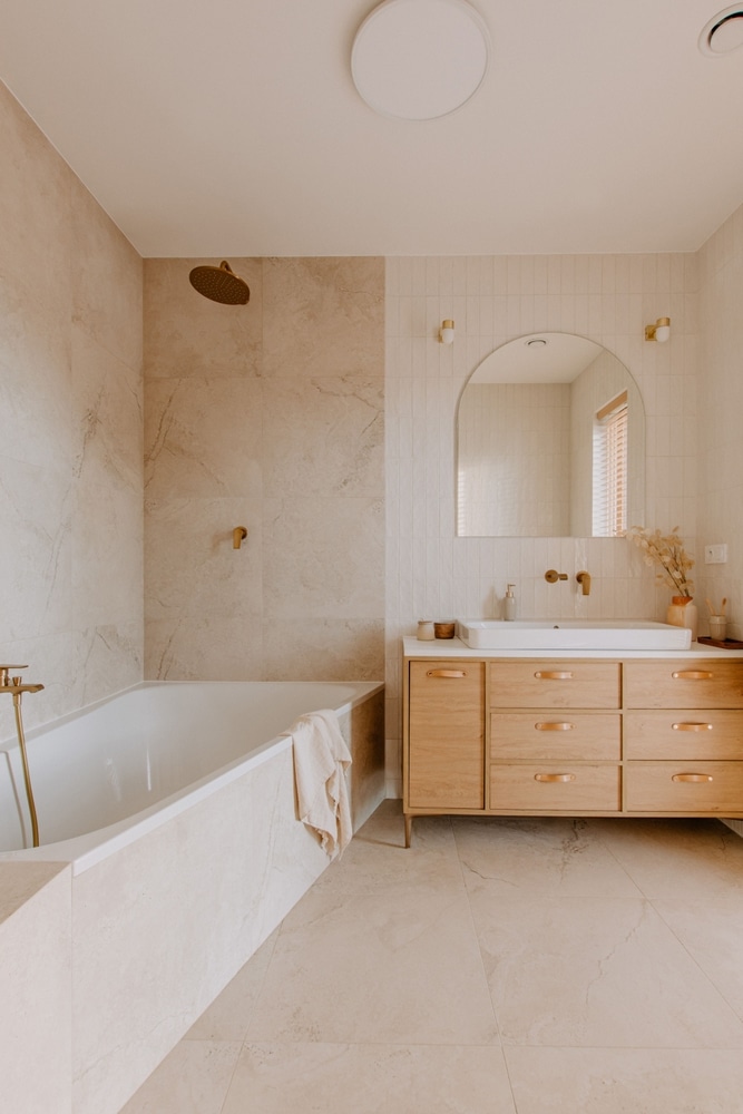 Salle de bain moderne beige et bois : Style minimaliste Salle de bain minimaliste aux tons beiges avec baignoire, vanité en bois, miroir cintré et robinetterie en laiton.